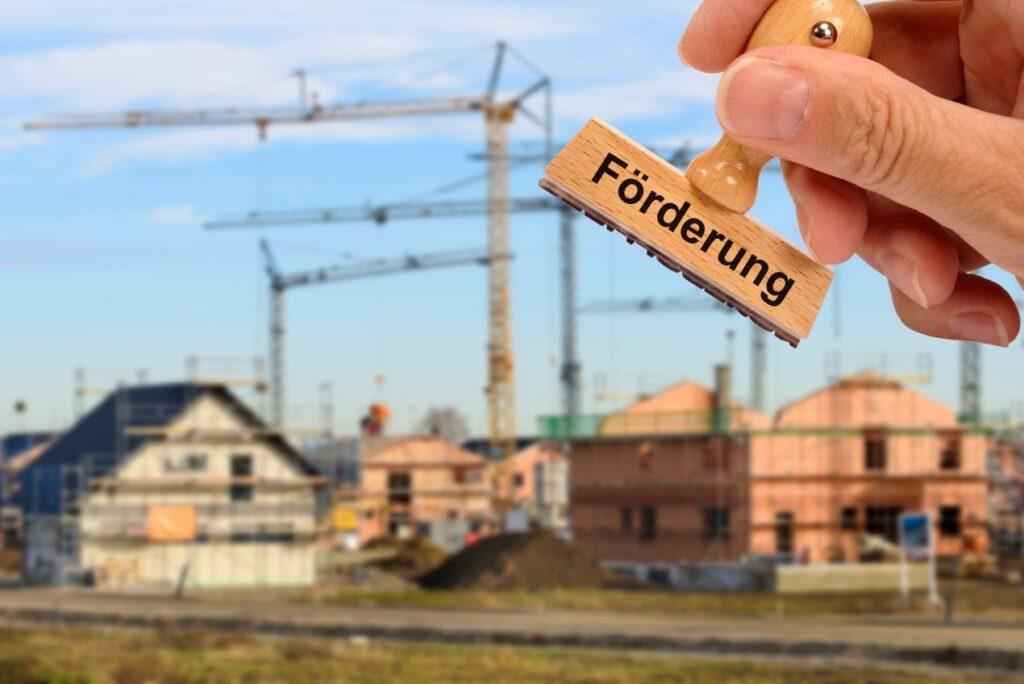 Baufoerderung fuers Eigenheim – Symbolbild mit Stempel und Neubauten im Hintergrund im Kontext der Steuerberatung Deggendorf